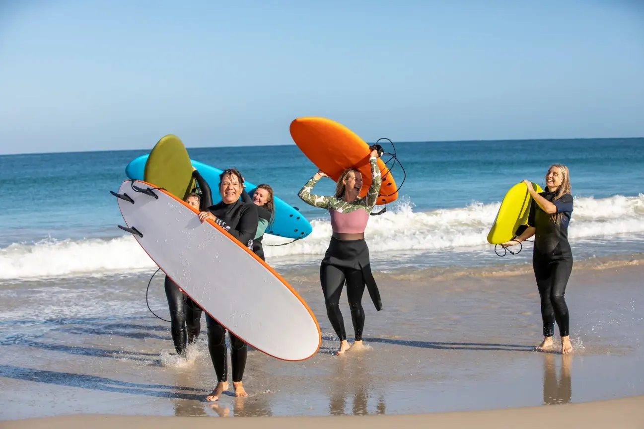 Aula de surf de grupo numa praia de Cascais — Dia 3 de uma viagem de incentivo da BTQ Events, com licras e pranchas longas na costa atlântica de Cascais