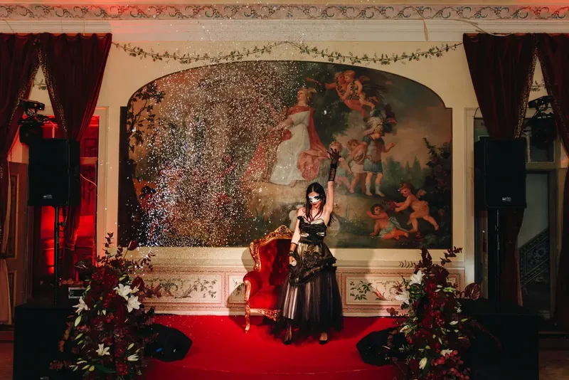 Artista mascarado no palco com passadeira vermelha, diante da sala com frescos do Palácio do Grilo