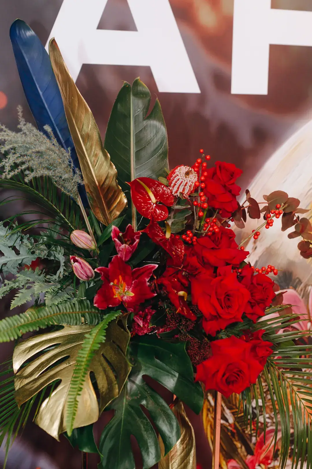 Composição floral vermelha e dourada junto à parede de uma festa de Natal