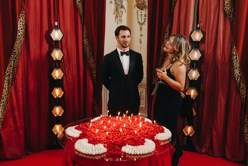 Convidado em black tie junto ao bolo de assinatura de framboesa e natas no aniversário do Palácio do Grilo