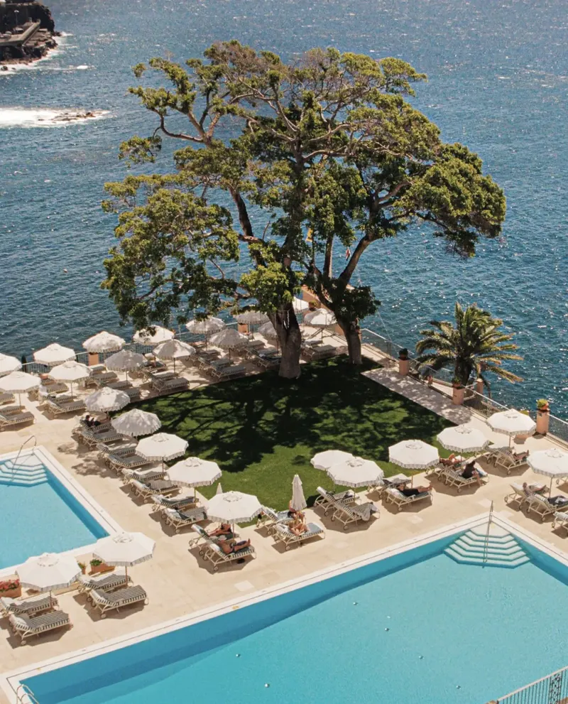 Belmond Reid's Palace iconic aerial · pool deck with single pine tree above the Atlantic at Funchal Bay