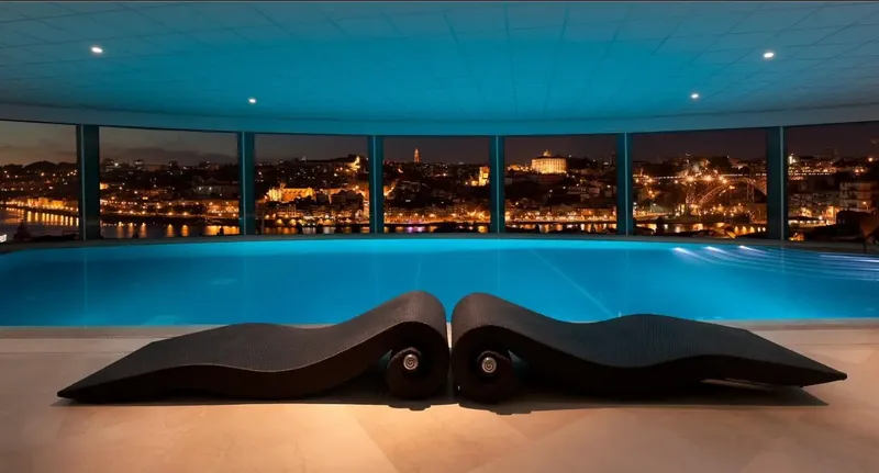 The Yeatman indoor infinity pool at night with Porto city lights through arched glass, part of the 2,000 m² Wine Spa with 10 treatment rooms used by BTQ Events as a wellness anchor inside multi-day corporate programmes